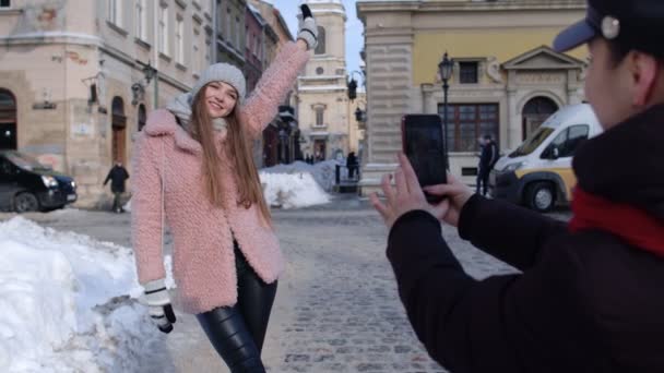 İki genç gülümseyen kadın gezgin blogcular şehir caddesinde cep telefonuyla fotoğraf çekiyorlar. — Stok video