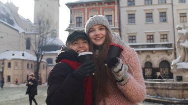 İki gülümseyen kadın turist birlikte seyahat ediyor, sıcak çay içiyor, şehirdeki bardaklardan kahve içiyor.