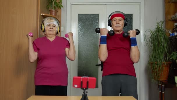 Pareja de ancianos mayores viendo ejercicios de entrenamiento en línea en el teléfono móvil y entrenamiento con pesas — Vídeos de Stock