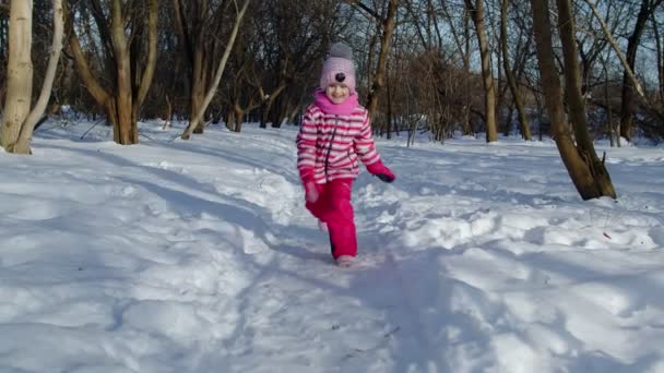 Menina criança alegre correndo em direção na estrada nevada, olhando para a câmera na floresta parque de inverno — Vídeo de Stock