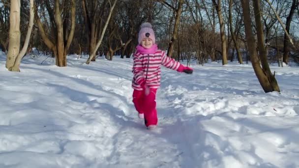 Dziewczynka biegająca po śnieżnej drodze, zabawiająca się, uśmiechnięta, patrząca w kamerę w lesie parku zimowego — Wideo stockowe