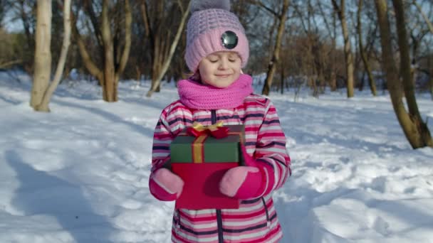 Радісна маленька усміхнена дівчинка, яка тримає різдвяну подарункову коробку в зимовому парку, Різдвяні свята — стокове відео