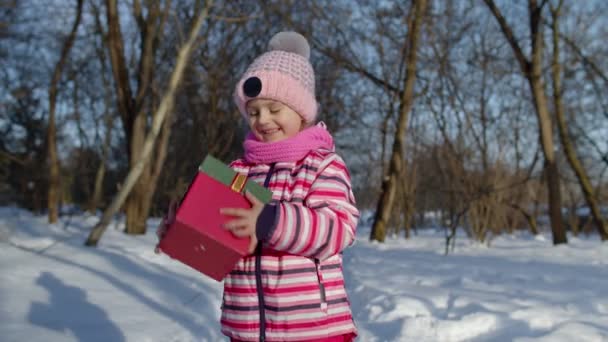 Joyeux sourire enfant fille regardant la caméra avec boîte cadeau de Noël dans le parc enneigé d'hiver — Video