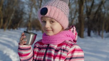 Çocuk, kış parkında, karlı yolda sıcak çay içiyor. Noel tatilinde.