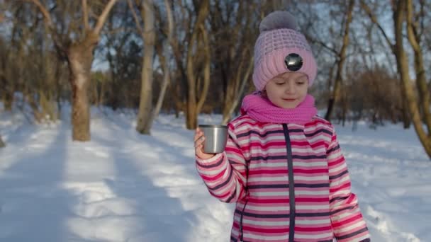 Sorrindo criança menina bebendo chá bebida quente da xícara, tentando manter o calor na floresta parque de inverno — Vídeo de Stock