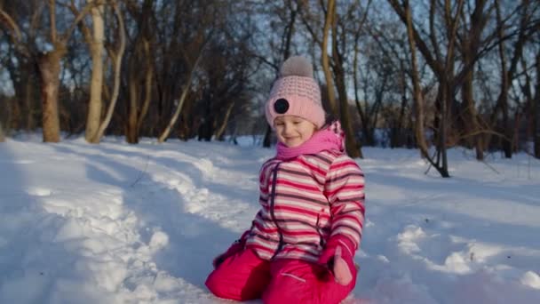 Radosna dziewczynka biegnie w kierunku zaśnieżonej drogi, patrząc w kamerę w lesie parku zimowego — Wideo stockowe