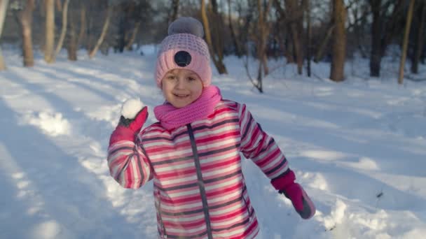 Дитяча дівчина кидає сніжку в камеру, усміхнений хлопчик ходить, грає зі снігом в зимовому парку — стокове відео