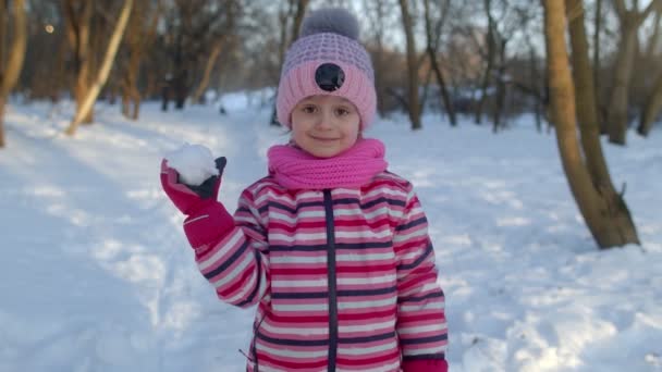 Vidám gyermek lány dobott hógolyó hópelyhek a kamerába, bolondozás körül, mosolyogva a téli parkban — Stock videók