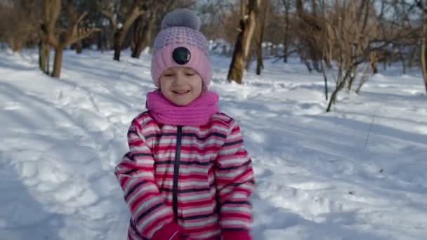 Kind meisje loopt op besneeuwde weg, rotzooien, glimlachen, kijken naar camera in winterpark bos — Stockvideo