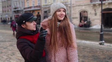 İki gülümseyen kadın turist kız kardeş. Şehir caddesinde birlikte yürürler. Aile çiftleri konuşur, kucaklaşır.