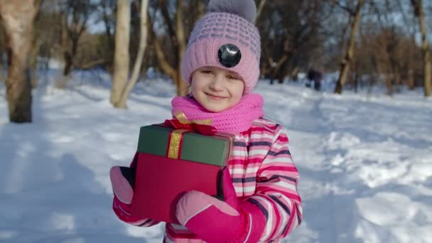 Wesoły uśmiech dziecko dziewczyna patrząc na aparat z pudełka prezent na Boże Narodzenie w zimie śnieżny park — Wideo stockowe