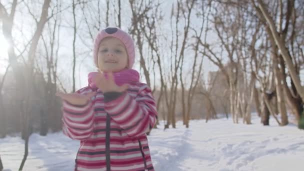 Gülümseyen çocuk, tamam işareti gösteriyor, gülümsüyor, dans ediyor, güneşli kış parkında, karlı yolda başparmağını kaldırıyor. — Stok video