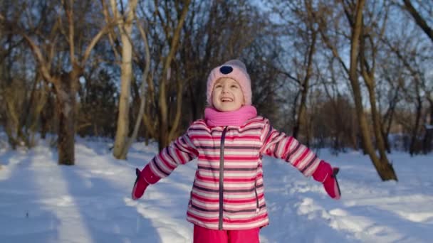 Niña alegre lanzando nieve, sonriendo, jugando, mostrando los pulgares hacia arriba en el bosque del parque de invierno — Vídeo de stock