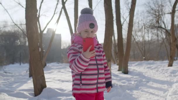 Barnflicka bloggare gör videosamtal på mobiltelefon, selfie foto för sociala nätverki vinterparken — Stockvideo