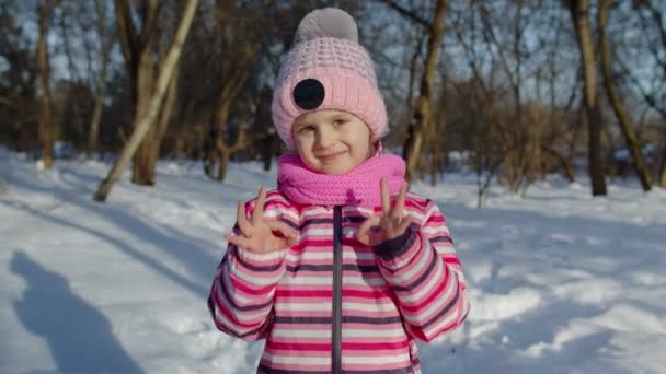 Niña sonriendo, mostrando señal de ok, pulgares hacia arriba gesto en el camino nevado en invierno bosque parque soleado — Vídeo de stock