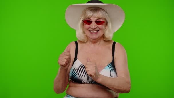 Ηλικιωμένη γυναίκα τουρίστρια με μαγιό και γυαλιά ηλίου, κοιτάζοντας την κάμερα, χαμογελώντας, δείχνοντας αντίχειρες προς τα πάνω — Αρχείο Βίντεο