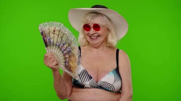 Пожилая женщина турист в купальнике бюстгальтер выдыхает от жары или душности, волны ручной вентилятор на себя — стоковое видео