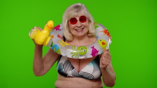 Starsza kobieta turystka w stroju kąpielowym tańczy, świętuje, bawi się nadmuchiwaną kaczą zabawką, gumowym pierścionkiem — Wideo stockowe