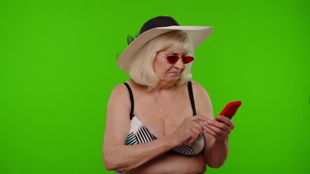 Starsza kobieta turystka przeglądająca aplikację na telefon komórkowy, poszukująca hotelu kurortowego na tle klucza chroma — Wideo stockowe