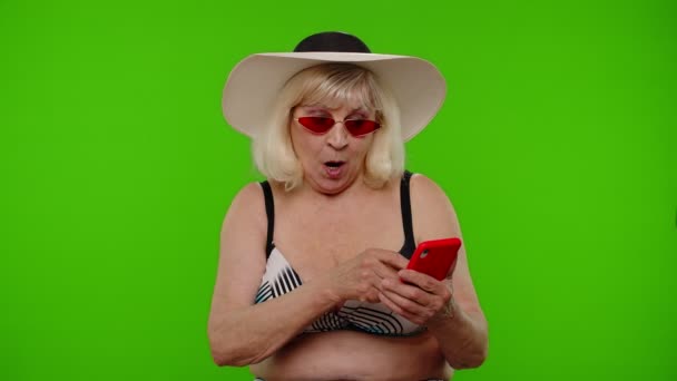 Зрелая женщина путешественница просматривает на мобильном телефоне и празднует победу отдых курорта — стоковое видео