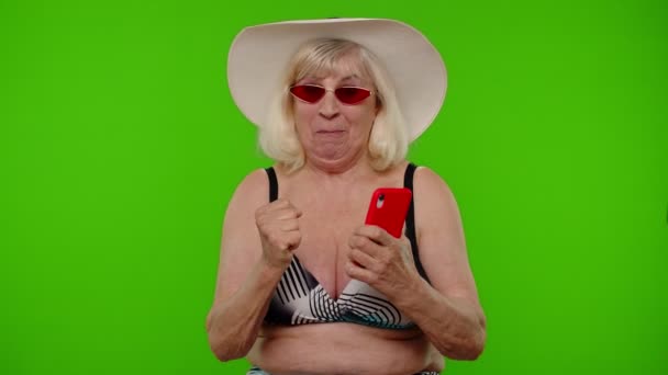 Seniorin mit Sonnenbrille und Handy feiert gewonnenen Urlaubsurlaub — Stockvideo