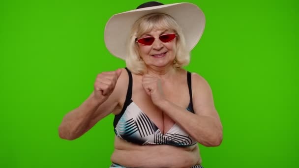 Starszy emerytka kobieta turysta w biustonosz strój kąpielowy, czerwone okulary przeciwsłoneczne i kapelusz taniec świętowanie, uśmiech — Wideo stockowe