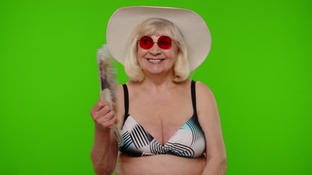 Senior old woman tourist exhales from heat or stuffiness, waves hand fan at herself on chroma key — Stock Video