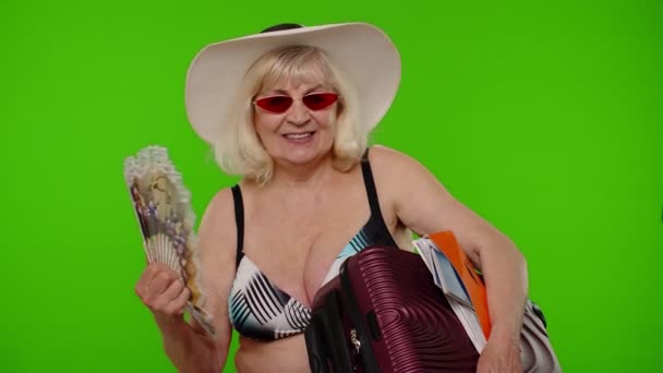 Senior old woman tourist exhales from heat or stuffiness, waves hand fan at herself on chroma key — Stock Video