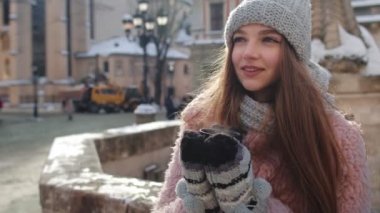 Sıcak bardakta sıcak içecekle şık bir kadın turist şehir sokaklarında tatil yaparken etrafa bakıyor.