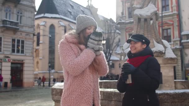 Dos mujeres turistas sonrientes viajando juntas, tomando té caliente, café del termo en la calle de la ciudad — Vídeo de stock