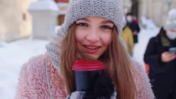 Chica turista con bebida caliente en la taza mirando a su alrededor a través de la calle en la ciudad durante las vacaciones — Vídeos de Stock