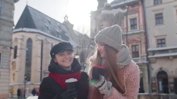 Dwie uśmiechnięte turystki podróżujące razem, pijące gorącą herbatę, kawa z kubków na ulicy miasta — Wideo stockowe