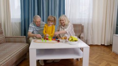 Torunlu büyük anne ve büyük baba oyun oynuyorlar, evde oyuncak trene biniyorlar.