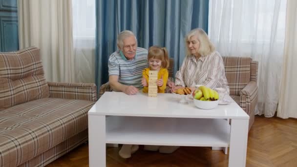 Senior couple grandparents with child kid granddaughter playing game with wooden blocks at home — Stock Video