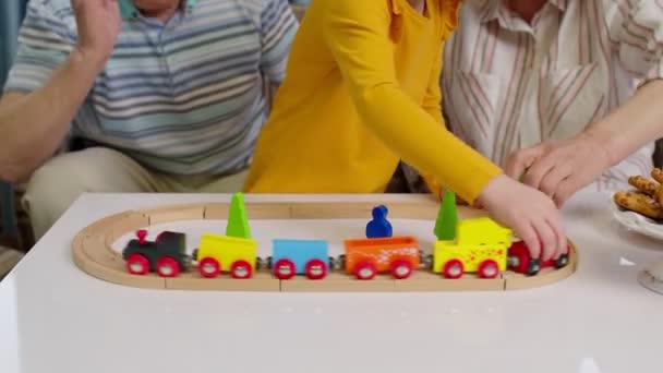 Senior-Großeltern mit Kind-Enkelin spielen Spiel, fahren Spielzeugeisenbahn auf Eisenbahn zu Hause — Stockvideo