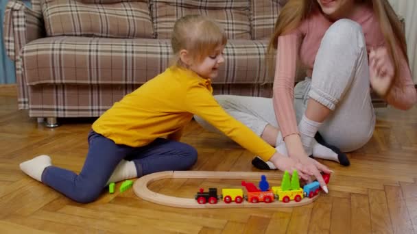 Mother playing with child kid daughter riding toy train on wooden railroad blocks board game at home — Stock Video