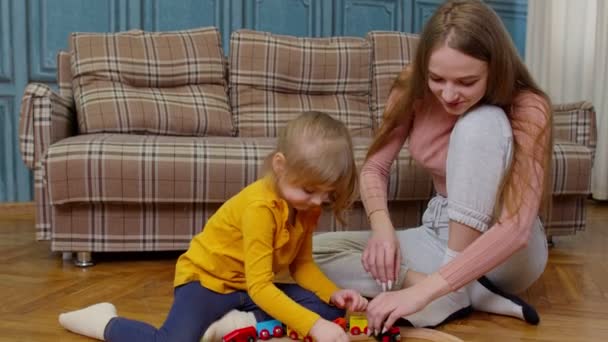 Moeder met dochtertje meisje paardrijden speelgoed trein op houten spoorweg blokken bordspel thuis — Stockvideo