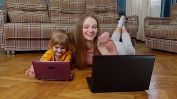 Mother and small daughter child sit on warm wooden floor at home working on laptop, watching cartoon — Stock Video