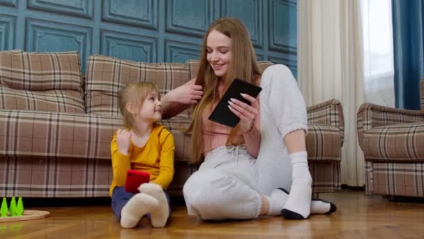 Mor och dotter barn sitter på golvet hemma arbetar på mobiltelefon och surfplatta, titta på tecknad film — Stockvideo