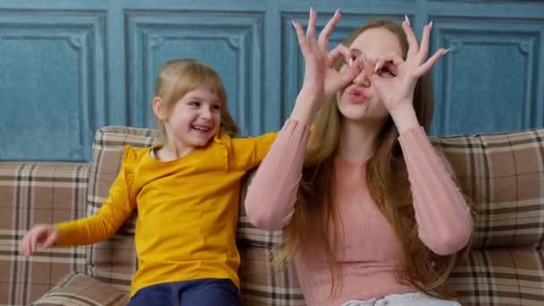 Moeder en klein kind kind dochter hebben plezier zitten op de bank rommelen rond, het maken van gezichten thuis — Stockvideo