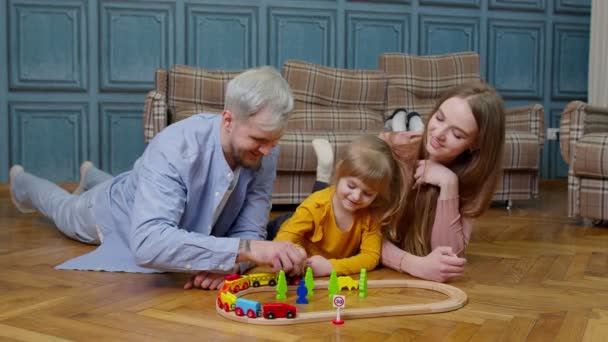 Young mother and father playing with child daughter riding toy train on wooden railroad game at home — Stock Video