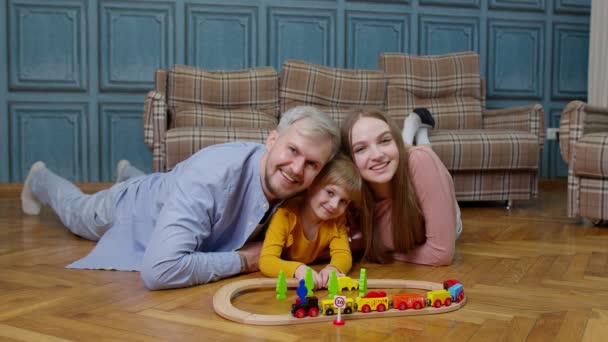 Joven madre y padre jugando con la hija del niño montar tren de juguete en el ferrocarril de madera juego en casa — Vídeo de stock