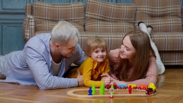 Familia de madre, padre con hija niña montando tren de juguete en tren de madera en la habitación de casa — Vídeos de Stock