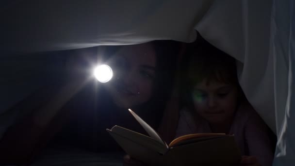 Ung mor läser godnattsaga saga till barn dotter under täcke filt i natt rum — Stockvideo