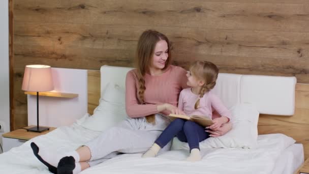 Jovem mãe e criança criança filha deitada na cama em casa, lendo livro histórias para dormir, contos de fadas — Vídeo de Stock