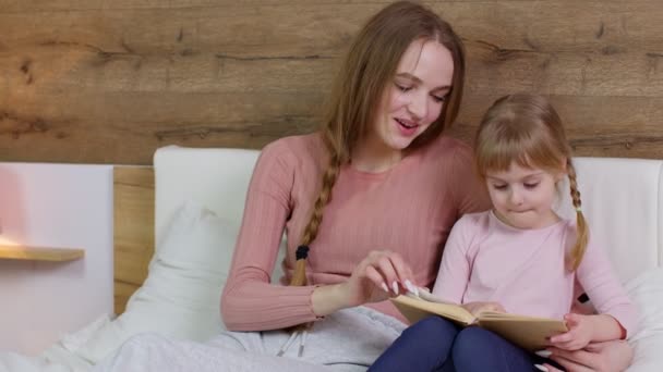 Ung mor läser godnatt berättelse bok saga till barn dotter flicka i natt sovrum — Stockvideo