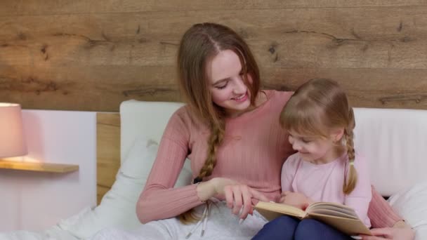 Young mother and child kid daughter lying in bed at home, reading book bedtime stories, fairytales — Stock Video