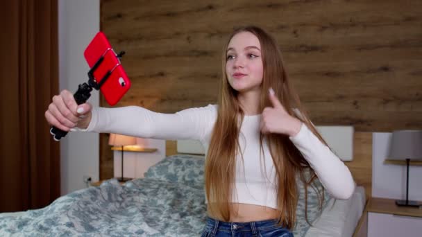 Gülümseyen sevimli vlogger kızı cep telefonuna bakıyor, video çekiyor, evde selfie çekiyor. — Stok video