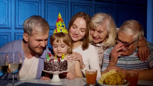 Чарівна дитина дівчинка їсть торт роблячи бажання, розважаючись, святкуючи день народження з сім'єю — стокове відео