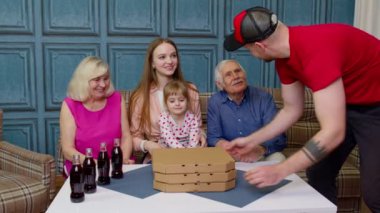 Fast food kutularıyla teslimatçı, sıcak pizzayı büyük, çoklu nesil bir ailenin önüne koyuyor.